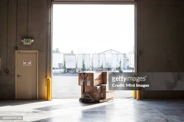a small stack of products in boxes sitting on a manual pallet jack in a loading dock door at a distribution warehouse. - pallet industrial equipment fotografías e imágenes de stock