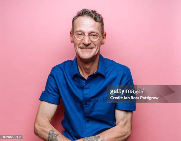 middle-aged man in blue shirt on pink background - pink shirt stock pictures, royalty-free photos & images