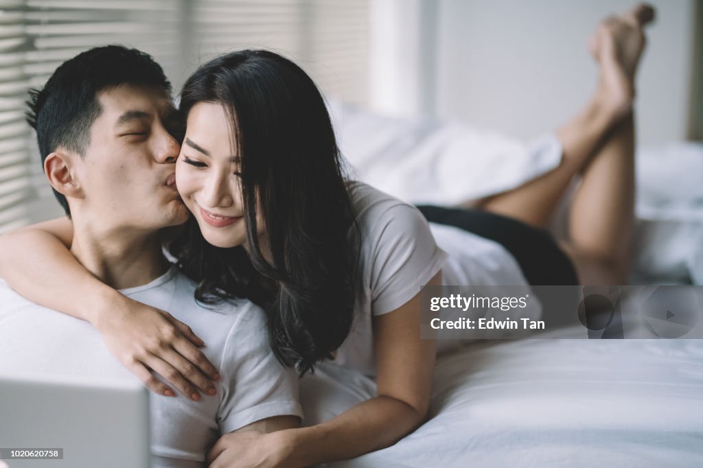 Asian chinese couple on bed in the morning having bonding time using laptop surfing internet