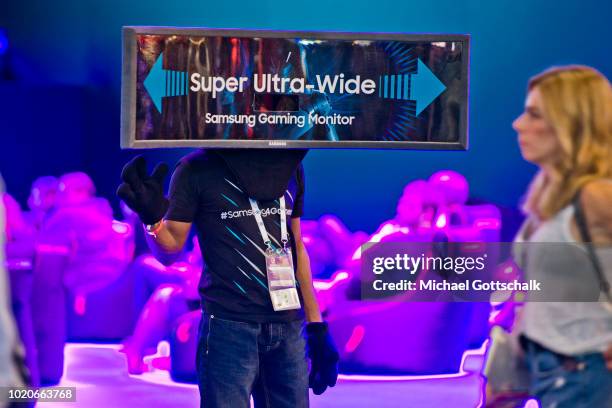 Steward wears a super ultra wide videoscreen on his head to guide visitors to Samsung booth at 2018 gamescom fair press day on August 21, 2018 in...
