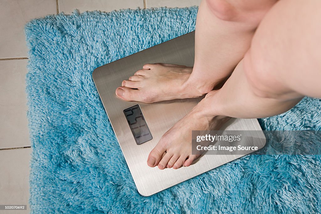 Young woman weighing herself on bathroom scales