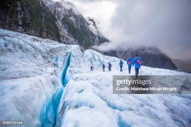 travelers explore new zealand's famous franz josef glacier. blue ice, deep crevasses, caves and tunnels mark the ever changing ice. - neuseeland stock-fotos und bilder