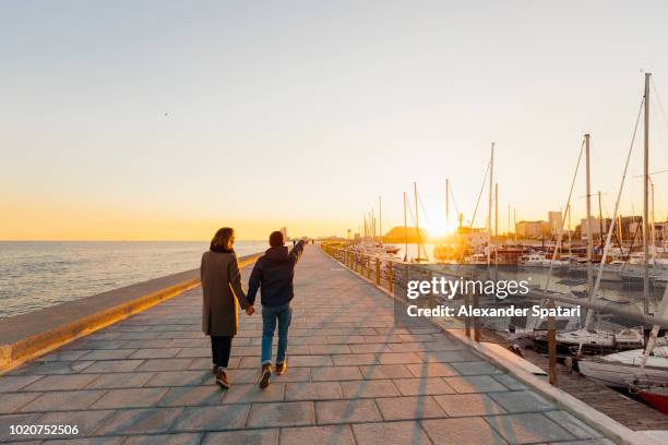 young couple holding hands walking towards sunset in barcelona, spain - barcelona winter stock-fotos und bilder