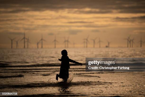 Young muslim girl dances and runs in the sea as she and her family celebrate Eid Al-Adha by watching the sunset at Crosby beach on August 21, 2018 in...