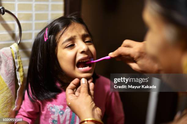 young girl crying while grandmother brushes her teeth - learning generation parent child photos et images de collection