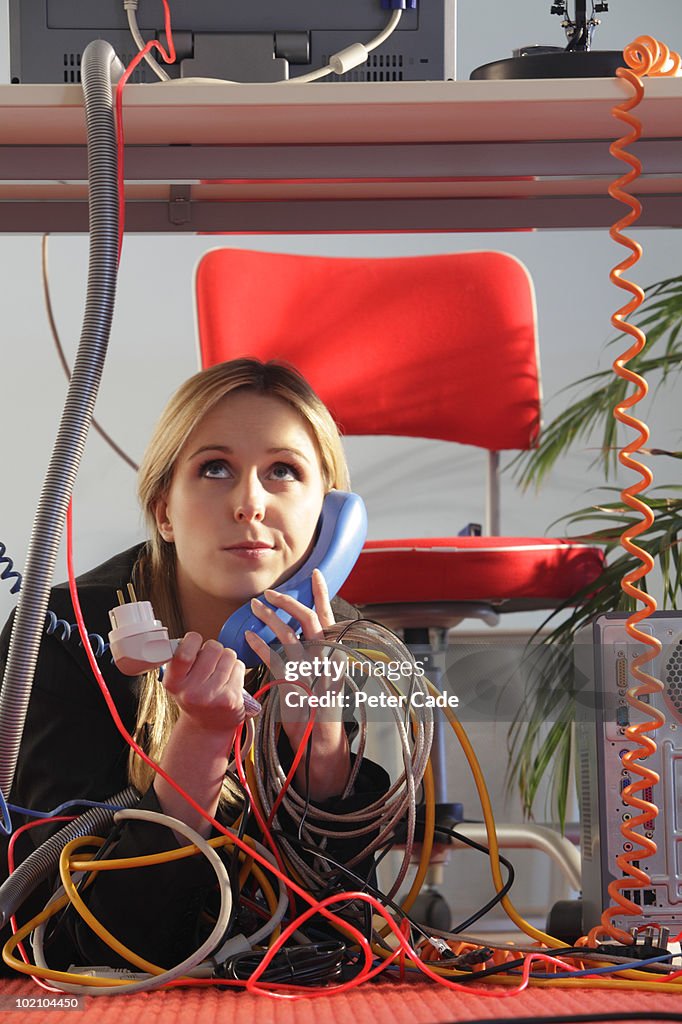 Woman under desk on phone with wires