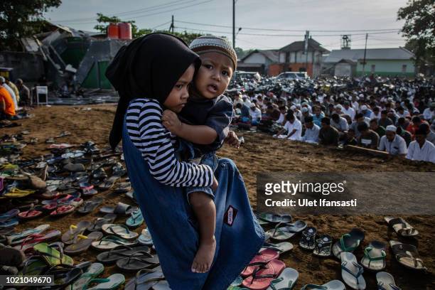 Girl carries her brother as they perform Eid al-Adha prayer near the damage houses in Pemenang on August 22, 2018 in Lombok island, Indonesia....