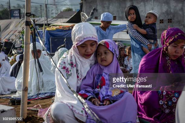 Girl carries her brother as they perform Eid al-Adha prayer near the damage houses in Pemenang on August 22, 2018 in Lombok island, Indonesia....