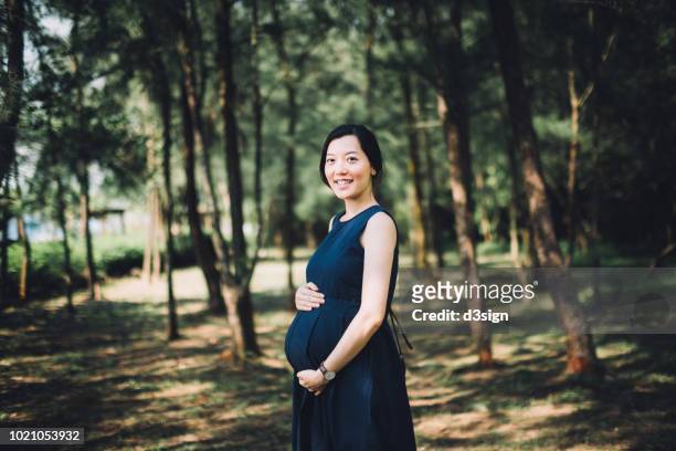 beautiful pregnant woman holding her belly relaxing in nature park - asian woman pregnant stock pictures, royalty-free photos & images