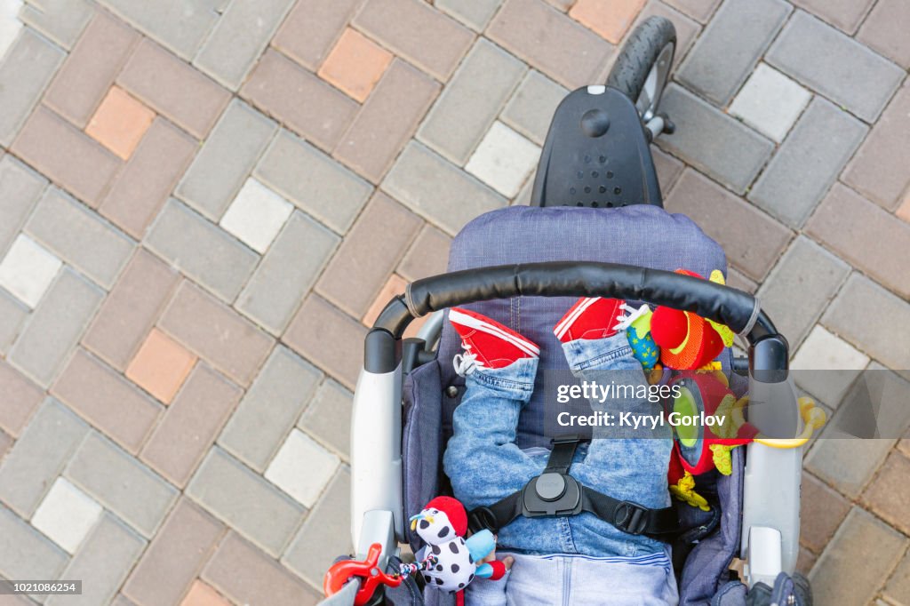 Baby sleeping three-wheel stroller outdoor. Child in bright casual costume lying at big comfortable pram. Parent walking with carriage in city park. View from above