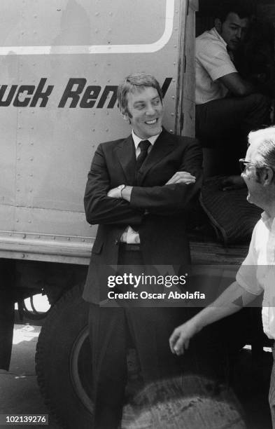 Canadian actor Donald Sutherland leans against a truck, his arms folded, circa 1975.