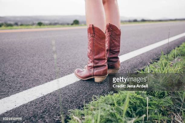 woman wearing cowboy boots side of road, wanderlust, travel, adventure, unrecognizable person, legs, concept waiting, conceptual waiting for opportunity, concept freedom - cowboystövlar bildbanksfoton och bilder
