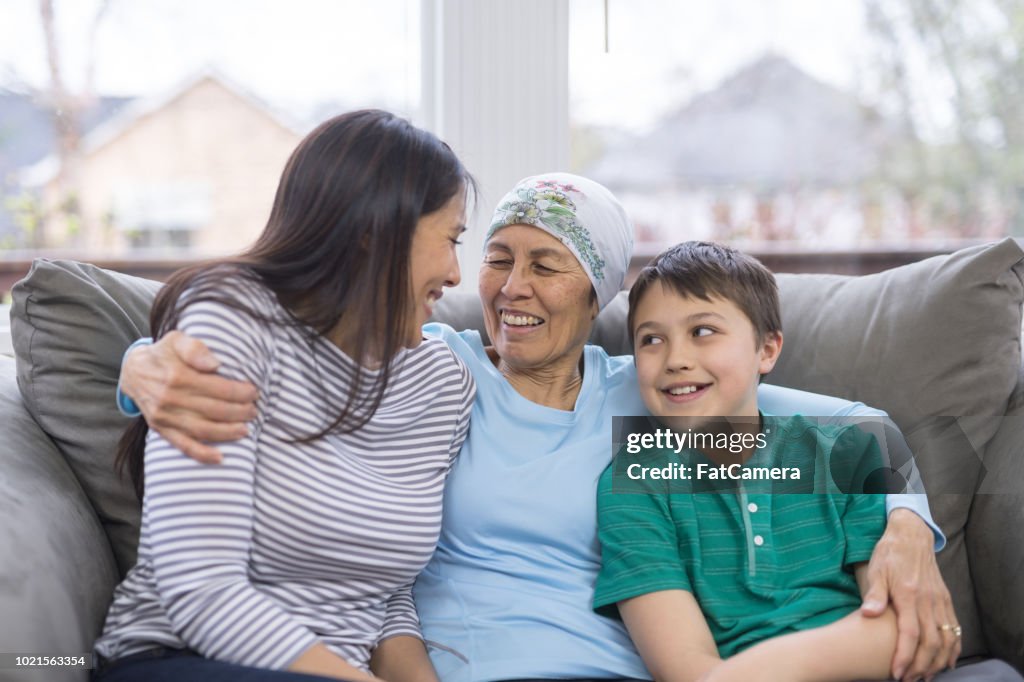 Uma mulher étnica em seu 60 anos lutando contra o câncer senta-se alegremente com sua filha e neto no sofá