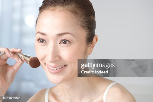 Mature woman applying powder on face with brush Mature woman applying powder on face with brush