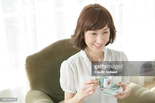 mature woman sitting sofa with a cup of tea - ボブヘア ストックフォトと画像