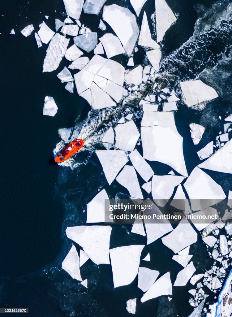 Wintery top-down aerial view of red ice-breaker pushing through cracked ice on Baltic Sea around Helsinki