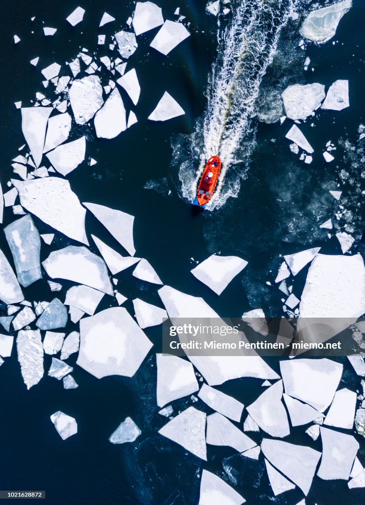 Wintery top-down aerial view of red ice-breaker pushing through cracked ice on Baltic Sea around Helsinki