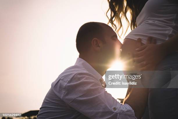 happy pregnant woman and her husband on the beach - belly kissing stock pictures, royalty-free photos & images