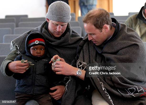 Prince Harry and Prince William put gloves on a young boy during a visit to a child education centre on June 17, 2010 in Semonkong, Lesotho. The two...