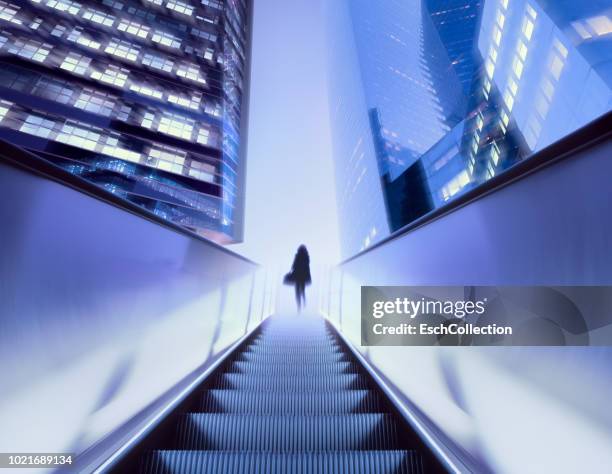 businesswoman on top of moving escalator at illuminated business district - al centro foto e immagini stock
