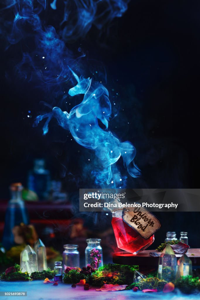 Unicorn silhouette made from smoke rising from a red potion bottle. Magical still life with witch or wizard workplace, dark background and copy space