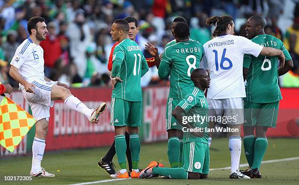 Vassilis Torosidis of Greece gestures with his leg while players argue with referee Oscar Ruiz as Sani Kaita of Nigeria kneels on the ground after...