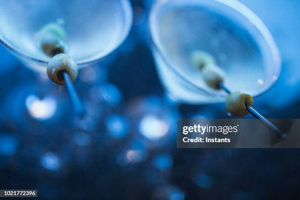 beschoten nacht in nassau, in blauw licht, twee dirty martini's met olijven permanent onder ijsblokjes. - dirty martini stockfoto's en -beelden