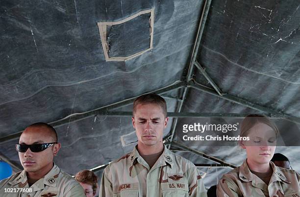 Navy Hospital Corpsmen Joshua Saniel, William Cangemi, and Jessica Hall bow their heads in prayer before a ceremony to mark their organization's...