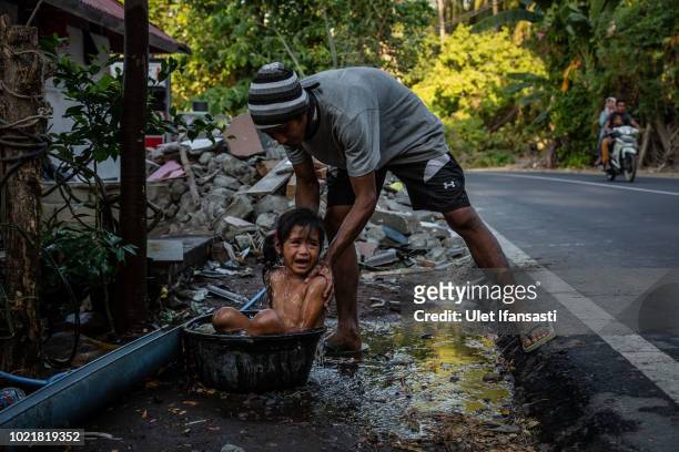 A man bathes his daughter as they clean the ruins of their damaged houses in Pemenang on August 23, 2018 in Lombok island, Indonesia. Thousands of...