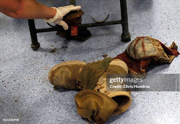 Medic removes the dirt-and-blood caked boots and equipment belonging to a wounded U.S. Soldier from under a gurney in the trauma bay at the Kandahar...