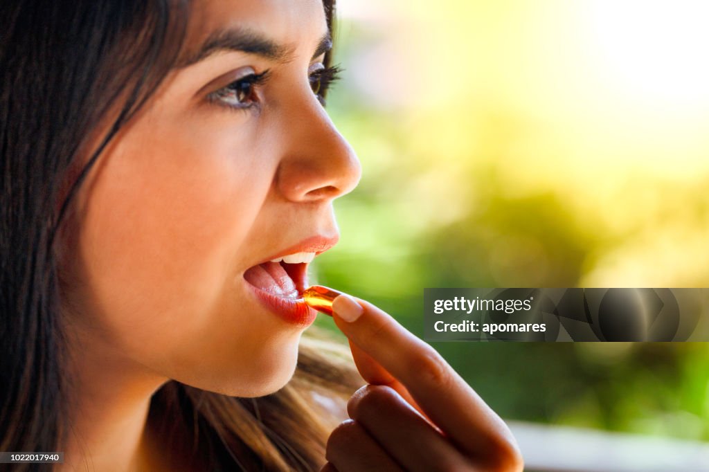 Hispanic young woman ready taking a pill with a glass of water in hand