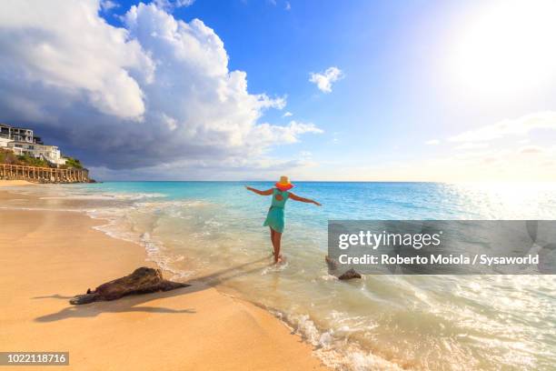 woman with hat and stretched arms enjoys the crystal sea, ffryes beach, antigua, antigua and barbuda, leeward islands, west indies - antigua leeward islands stockfoto's en -beelden