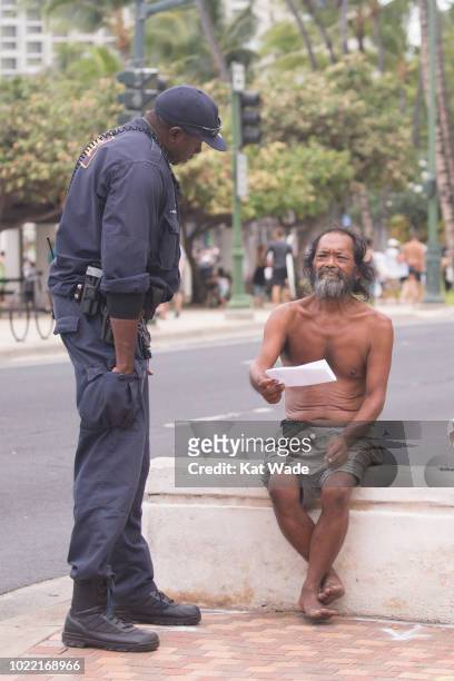 Honolulu police officer Cory Brailsford offers a homeless man a sheet with a list of shelters as Hurricane Lane approaches Waikiki Beach on August...
