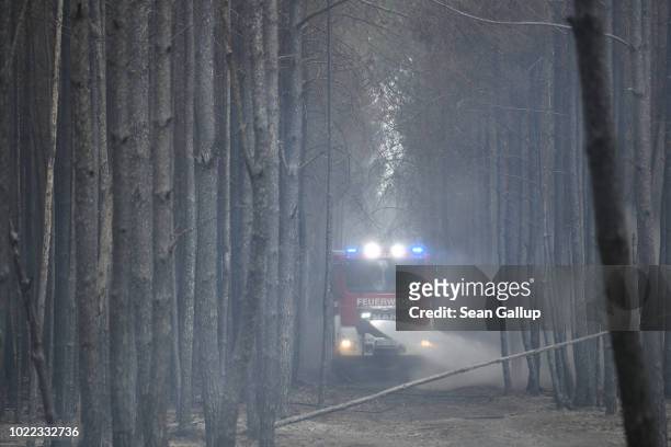 Firetruck squirts water into a smoldering section of forest in southern Brandenburg state on August 24, 2018 near Klausdorf, Germany. A fire covering...