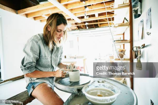 Woman spinning mug on potters wheel in garage studio