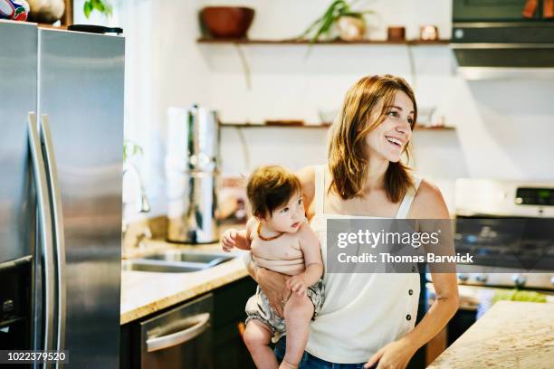 smiling mother holding infant daughter in home kitchen - kitchen fridge stock-fotos und bilder