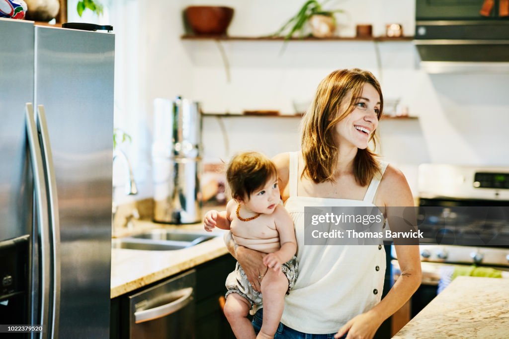 Smiling mother holding infant daughter in home kitchen