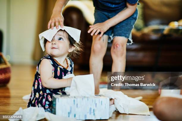 young boy putting facial tissue on infant sisters head in living room - tissue box stock-fotos und bilder