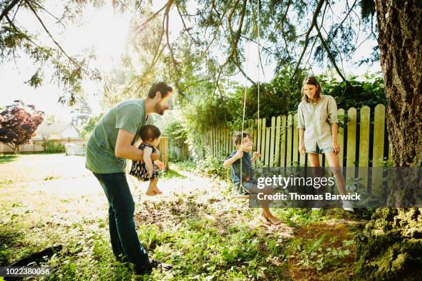 family hanging out together at swing in backyard on summer morning - playground equipment happy parent stock pictures, royalty-free photos & images