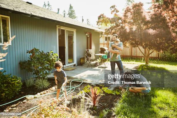 family watering garden in backyard on summer morning - day 4 stockfoto's en -beelden