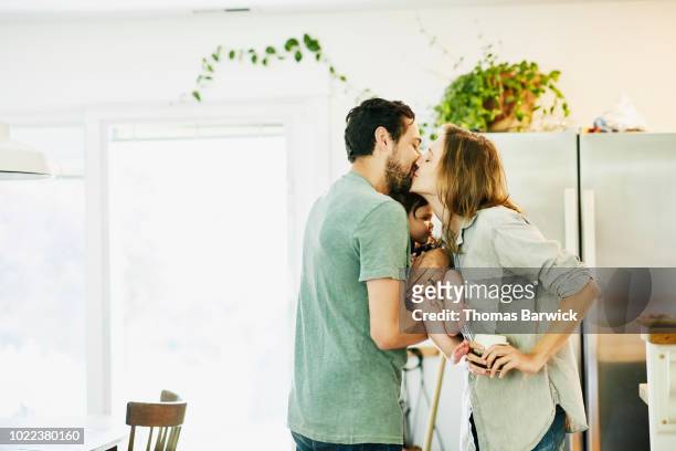 mother and father kissing while holding infant daughter in kitchen - bring to life stock-fotos und bilder