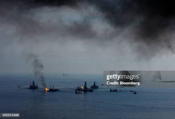 Smoke from controlled burns of oil on the surface of the water hangs in the air as the Development Driller II and III work on relief wells and the...