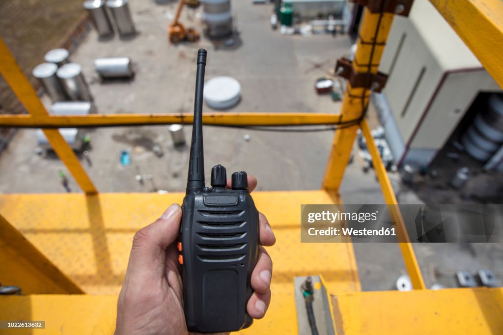 Hand holding walkie talkie on top of a crane on construction site