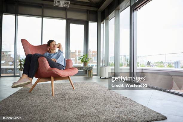 woman sitting in armchair at home relaxing - comfortable chair stock pictures, royalty-free photos & images