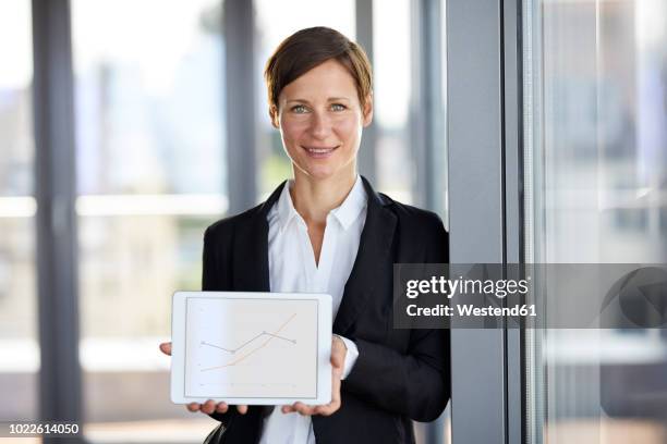 portrait of smiling businesswoman in office holding tablet showing ascending line graph - showing tablet stock pictures, royalty-free photos & images