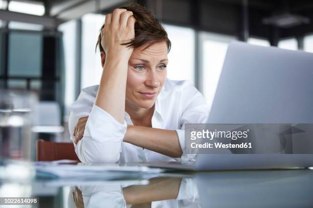 frustrated businesswoman sitting at glass table in office looking at laptop - delusione foto e immagini stock
