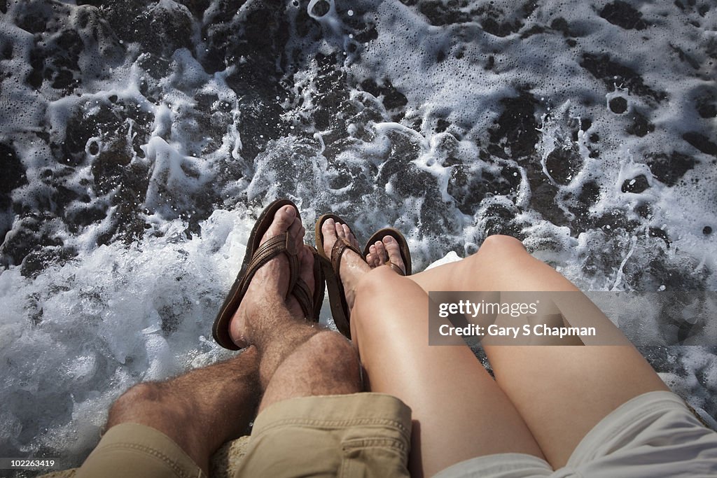 Hispanic couple's legs at ocean's edge