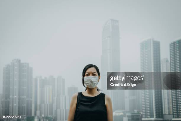 young woman wearing protective face mask in city due to the polluted air - luftverschmutzung stock-fotos und bilder