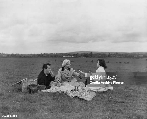 American actors Rock Hudson and Barbara Rush having a picnic with script supervisor Betty Abbott , on a stud farm owned by Prince Aly Khan, outside...