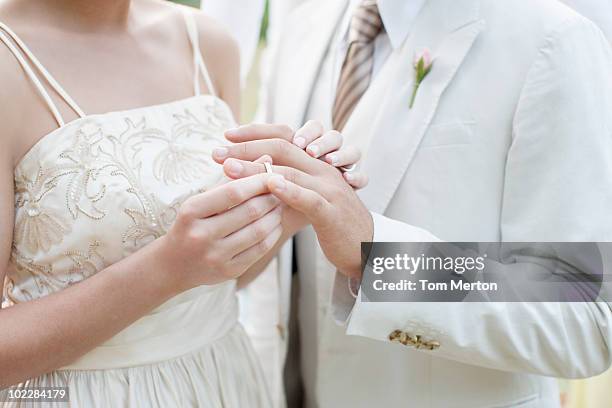bride putting ring on grooms finger - bruidegom stockfoto's en -beelden